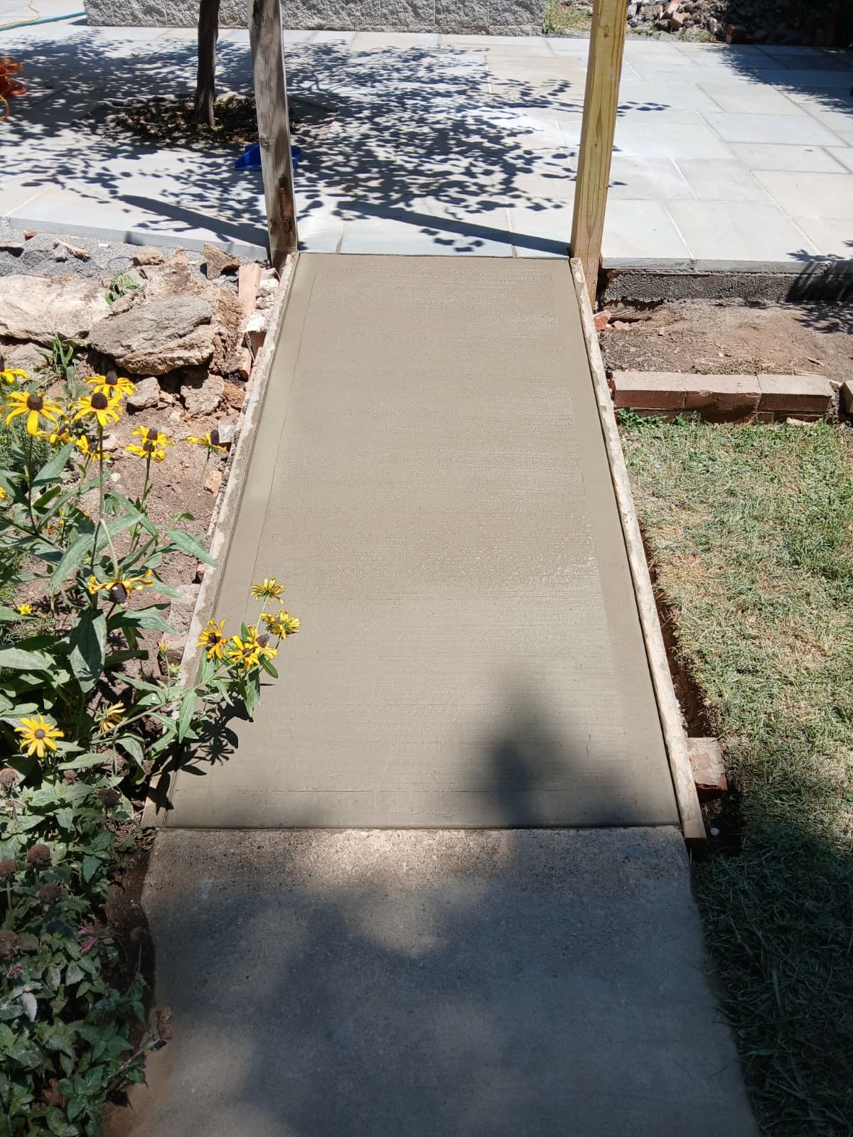 Freshly poured concrete walkway beside a bluestone flagstone patio