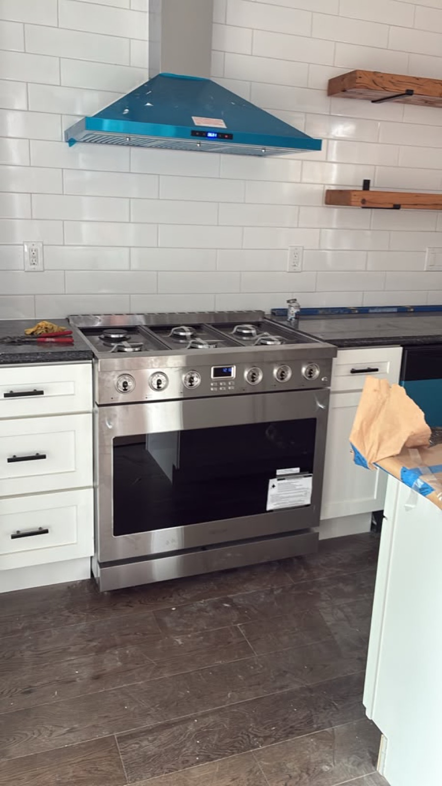 Pro-style range with teal vent hood, subway tile, and wood shelves