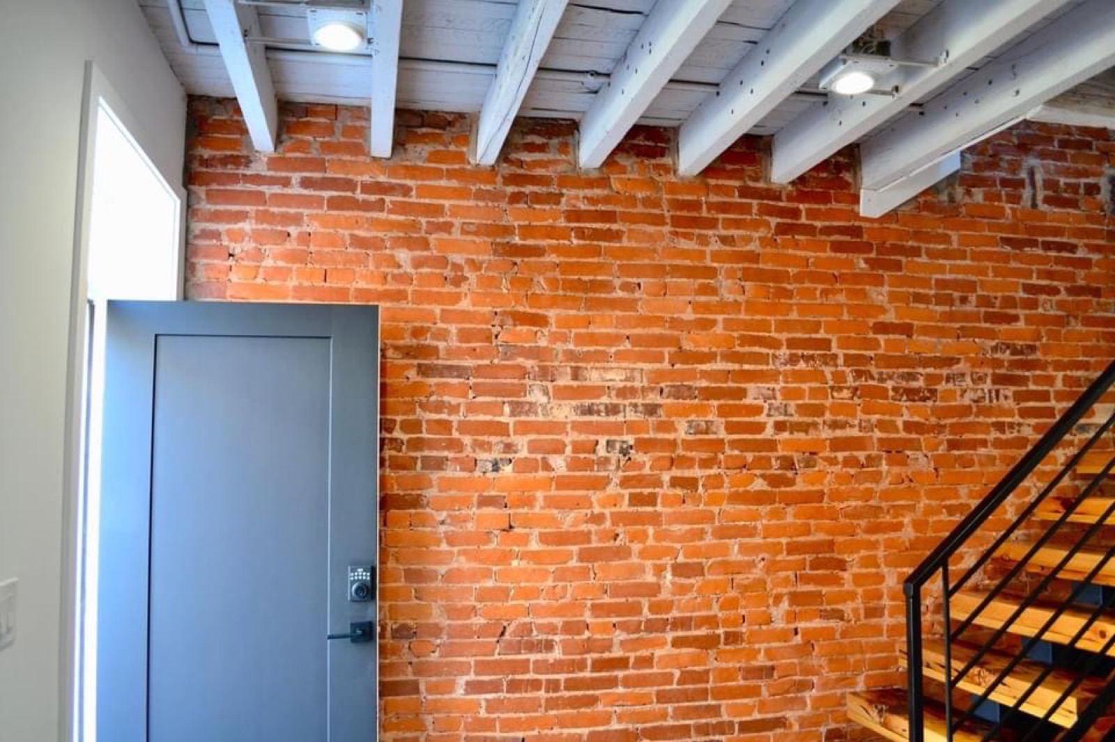 Entry door against exposed brick under a whitewashed joist ceiling