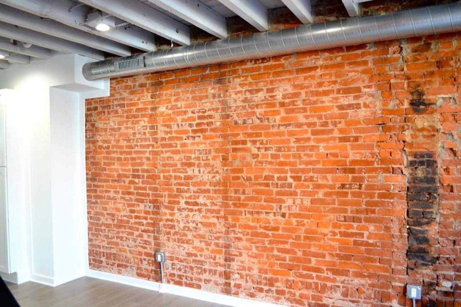 Living room with full exposed brick wall, spiral duct, and whitewashed joists
