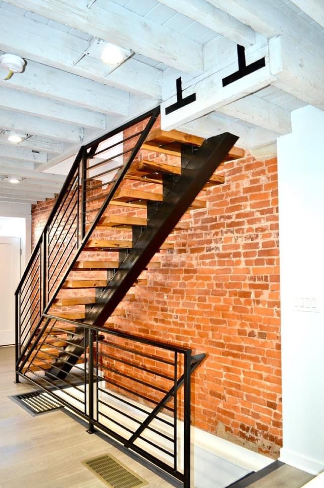 Floating steel-and-reclaimed-wood staircase against exposed brick