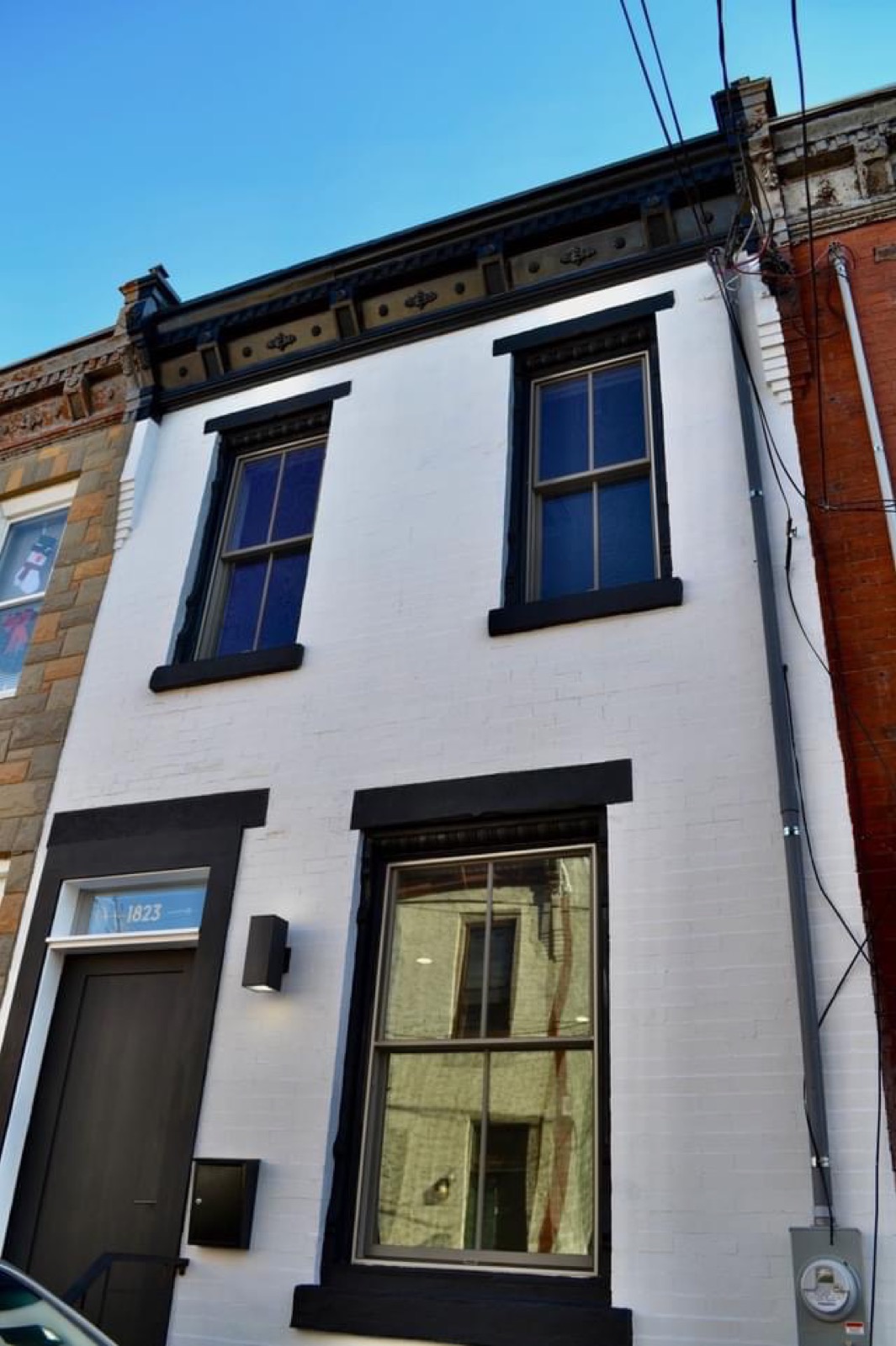 Renovated rowhome facade with white-painted brick, black windows, and restored cornice