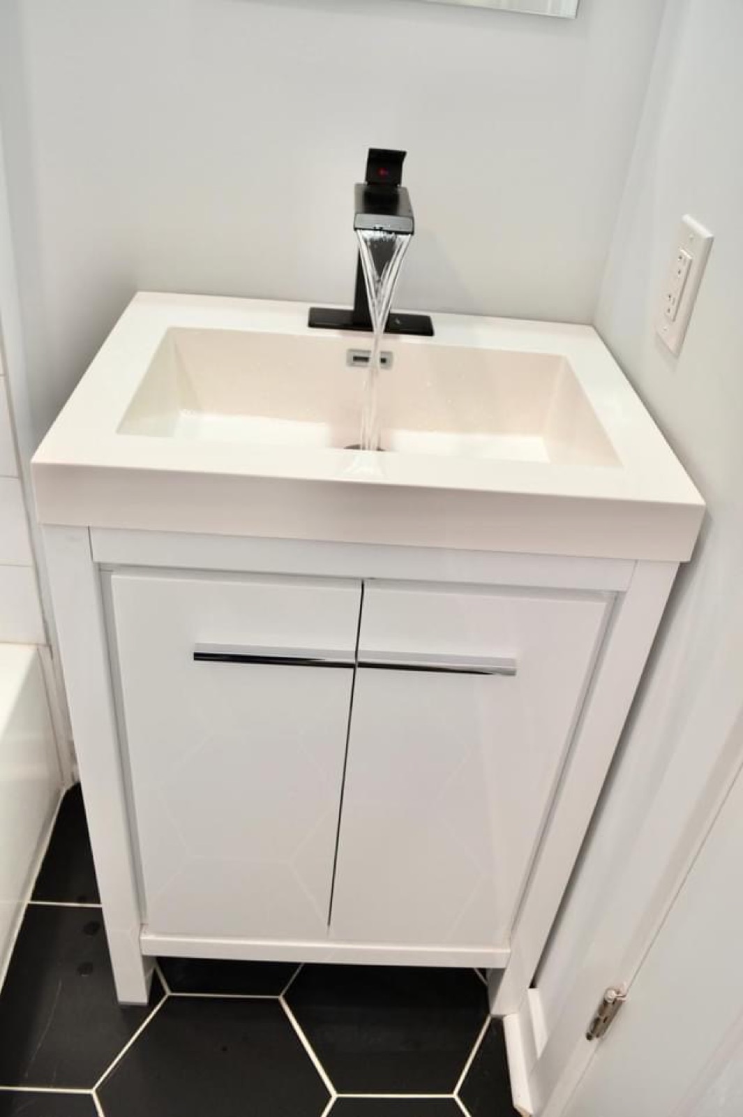 White vanity with waterfall faucet over black hexagon tile