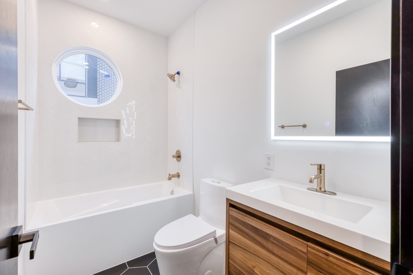 Guest bath with herringbone tile tub surround, round window, and walnut vanity