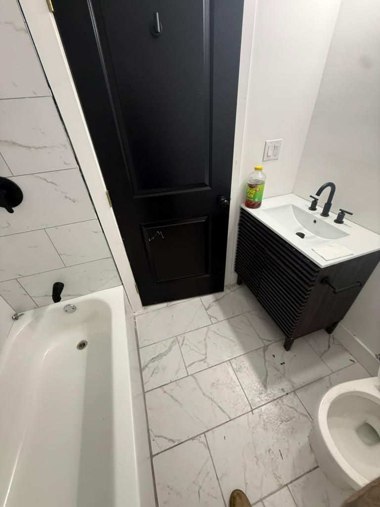Black fluted vanity with white top on a marble-look tile floor beside the tub