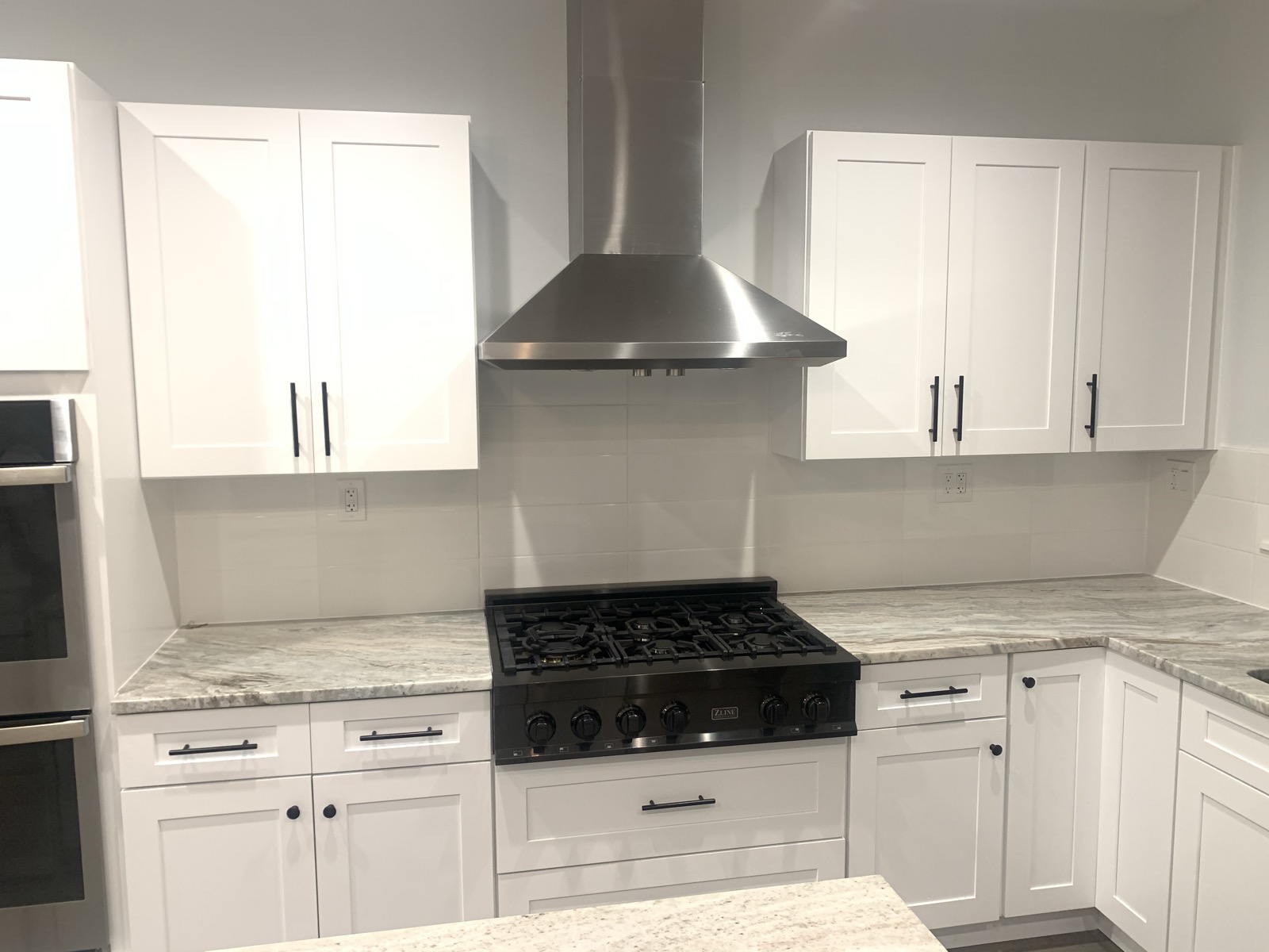 Stainless chimney hood over a gas range with white shaker cabinetry