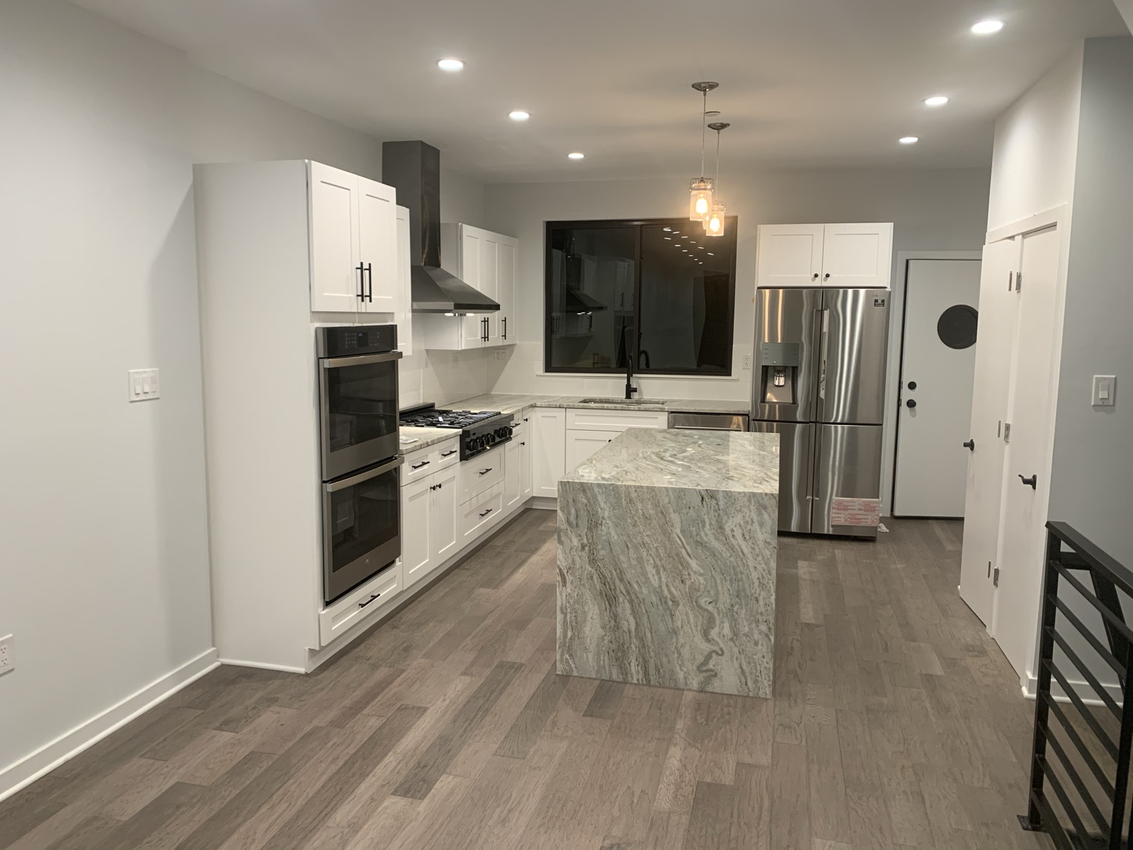 Wide kitchen view with island, stair railing, and hardwood floors