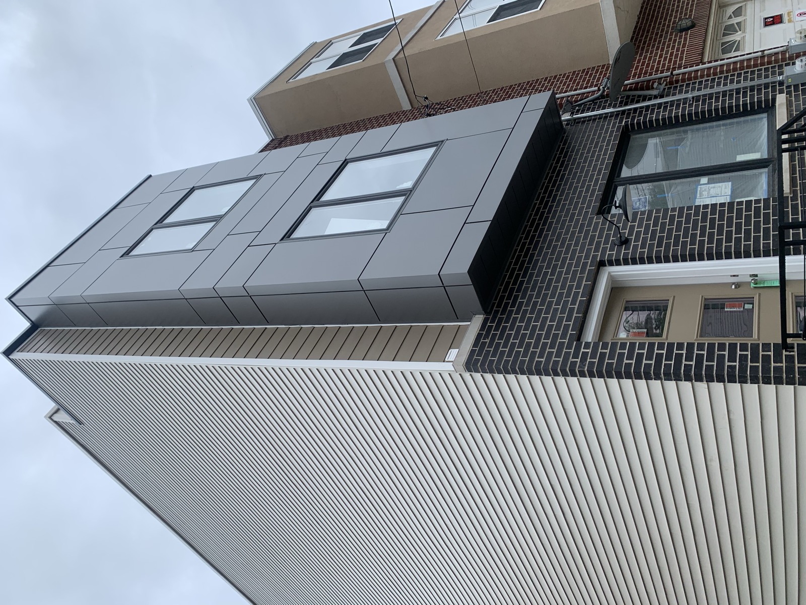 Three-story new construction townhome facade with gray panels and black brick