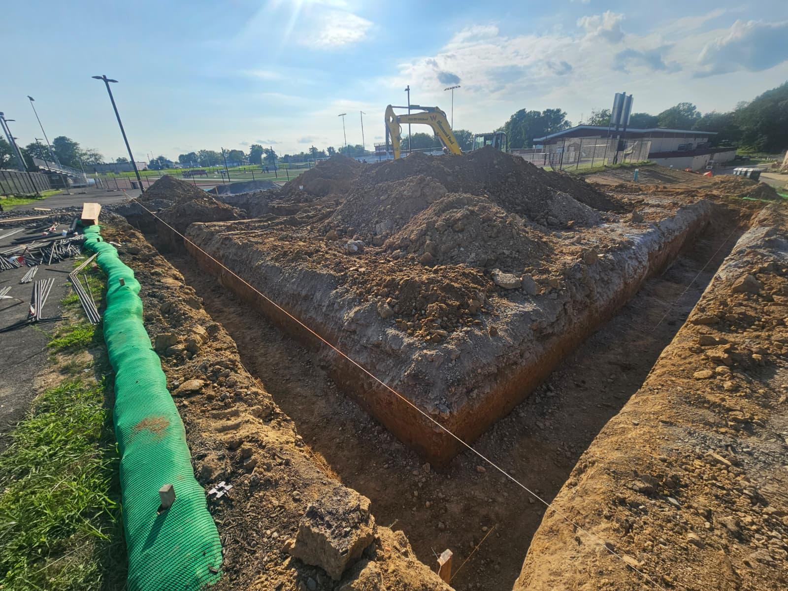 Footing trenches excavated and strung for layout, with a silt sock in place