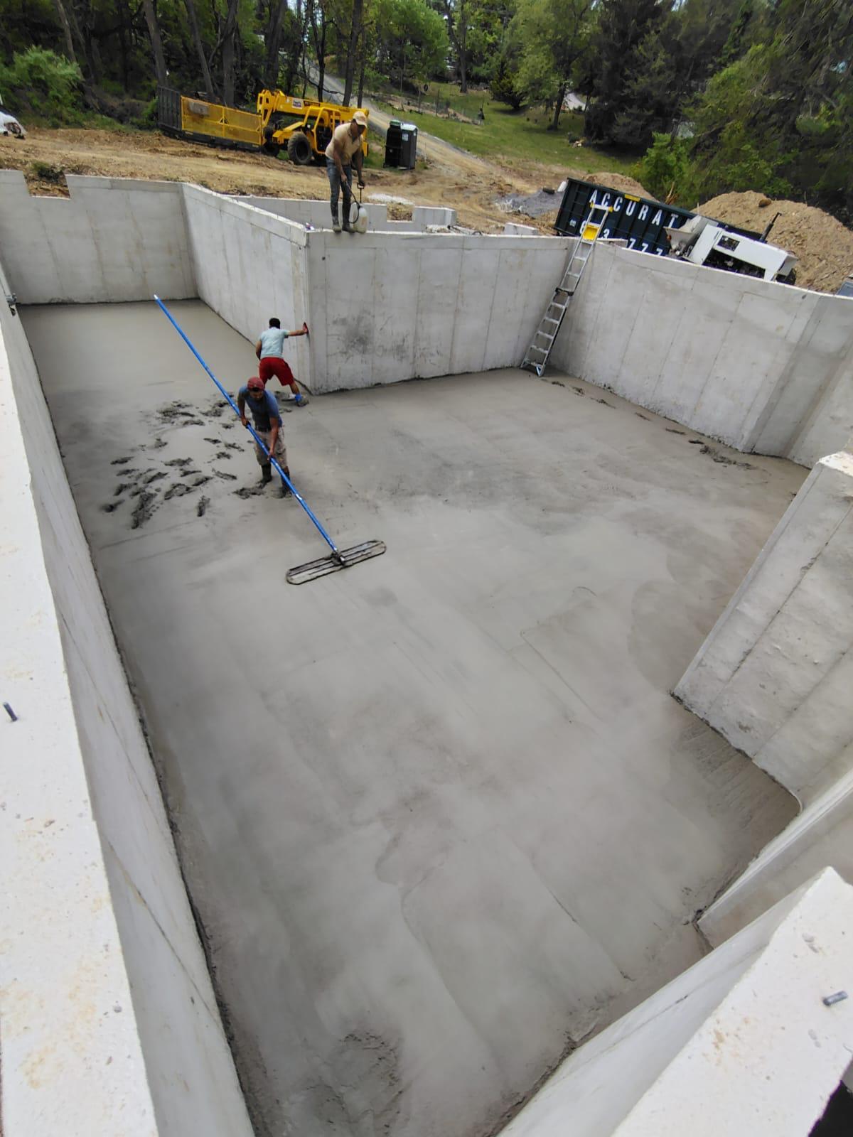 Crew screeding a basement slab inside poured concrete foundation walls