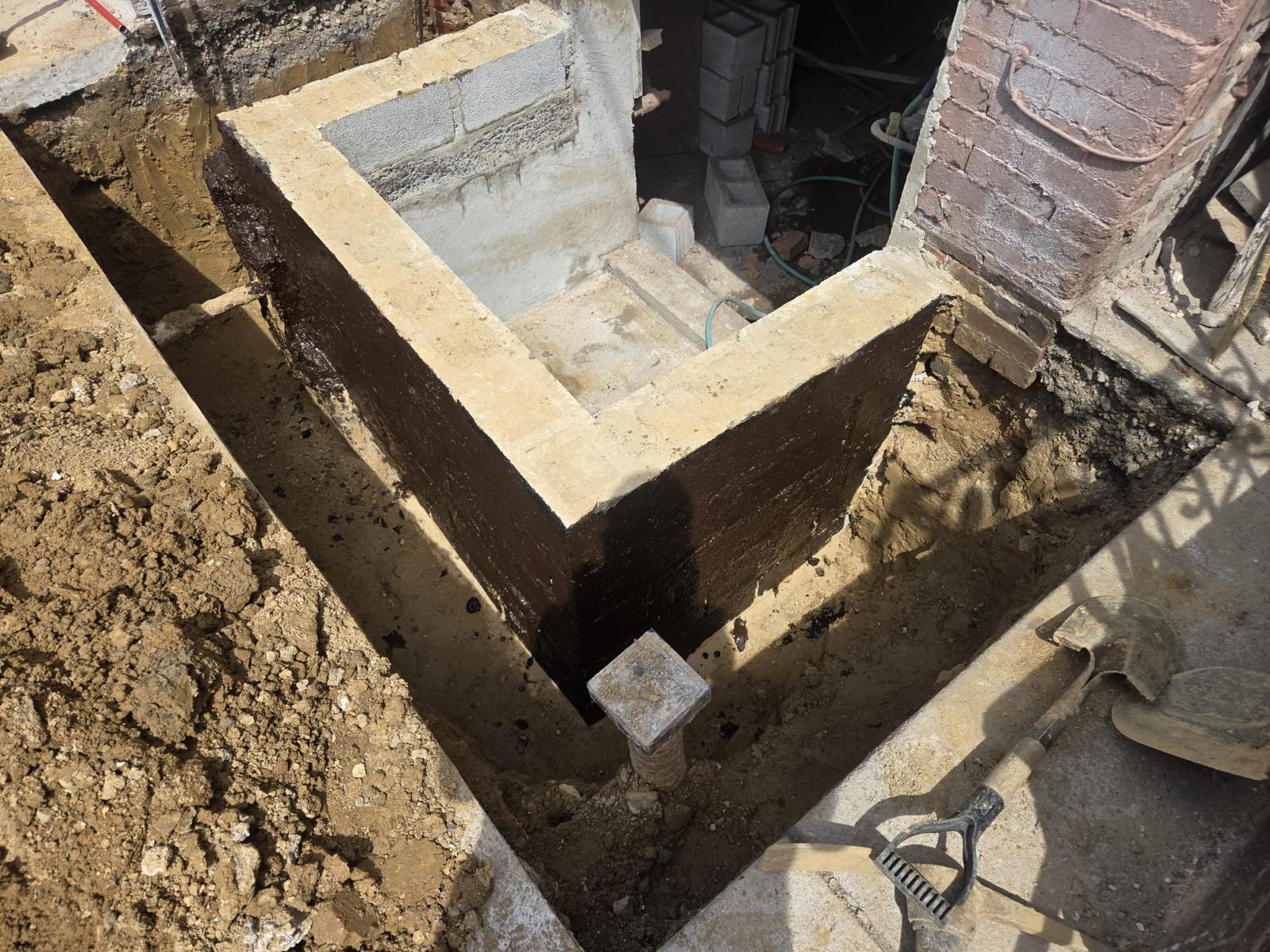Poured concrete foundation wall with waterproofing beside a brick rowhome
