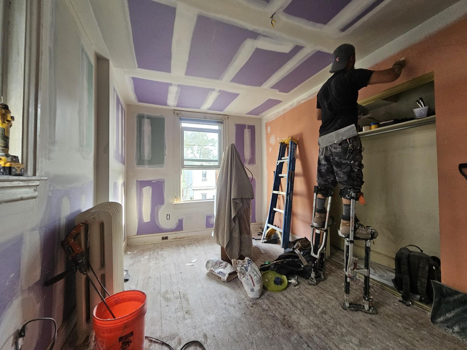 Drywall finisher on stilts taping new board in the bedroom