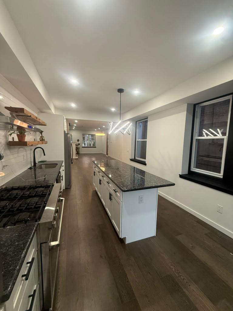 Kitchen with floating wood shelves, subway tile backsplash, and granite island