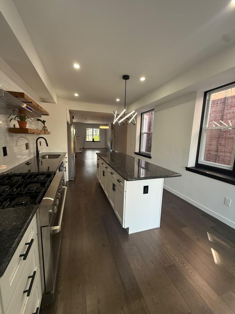 Black granite island and gas range in the white shaker kitchen